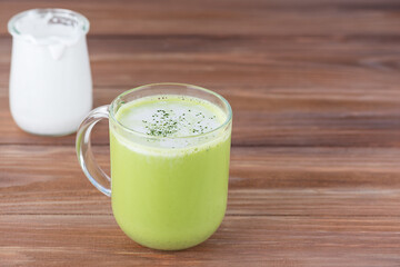 Matcha latte tea with coconut milk and hemp seeds in a glass mug on a wooden table.