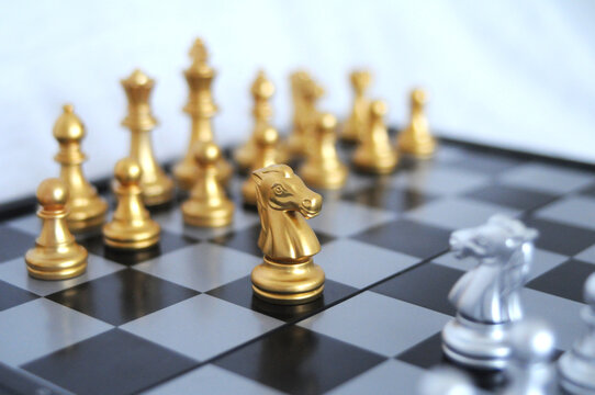 Golden horse chess encounters with silver horse enemy on chess board and white background. Market or business competitor concept.