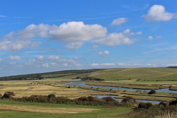 Obraz premium Cuckmere River and valley seen with blue skies and fluffy white clouds (East Sussex, United Kingdom) 