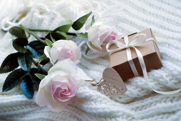 three roses, gift box, wooden heart on the background of a white knitted scarf. a gift with love. romantic background, valentine's day card. congratulations on March 8. cozy scene. 