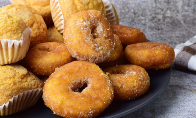 Donuts with sugar and muffins, on a dark plate on a stone background.