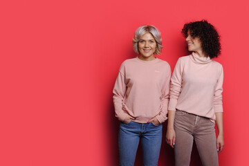 Portrait of two smiling caucasian women standing against pink background with copyspace. - obrazy, fototapety, plakaty
