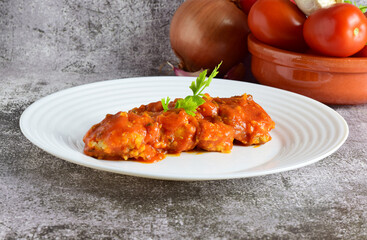 Cod fish with tomato sauce, garlic and parsley, served on a white plate.
Stone background and copy space.