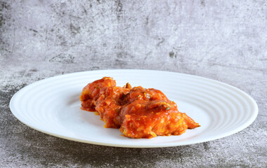 Cod fish with tomato sauce, garlic and parsley, served on a white plate.
Stone background and copy space.