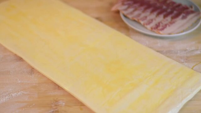 Putting smoked bacon slices on the sheet of raw puff pastry covered with egg wash. Making savory bakery product at home