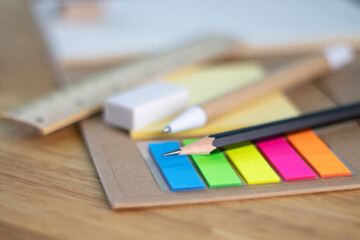 selective focus pencil for writing and multicolored square colorful sticky notes, rulers, and paper book on wood table concept equipment office and school