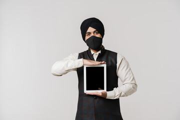 South asian man wearing turban and face mask showing tablet computer