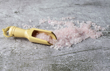 Close up, small wooden spoon with bath salts on gray stone background.