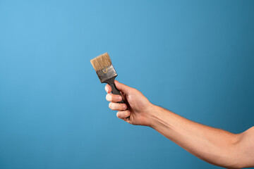 Update the interior, paint the walls, decor in the house. A man's hand stretches out a paint brush, blue background