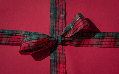 Winter holiday festive tartan pattern bow on the red background. Christmas wrapping gift box concept card.
