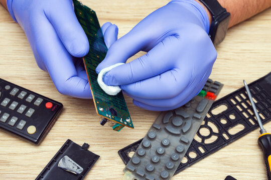A man in rubber gloves cleans the TV remote control from oxidation and dirt. Electronics repair at home.