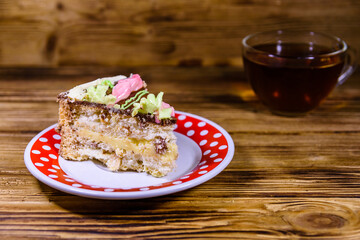 Cup of tea and plate with slice of Kiev cake with cream, nuts and meringue on a wooden table