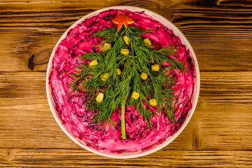 Ceramic plate with russian traditional new year salad herring under fur coat (shuba) decorated with christmas tree made from dill on rustic wooden table. Top view