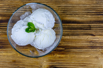 Glass bowl with ice cream balls and mint leaf on a wooden table. Top view