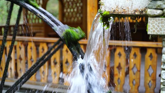 Water pours on the wheel of an old mill. The old wheel is overgrown with algae. Slow motion, close-up.