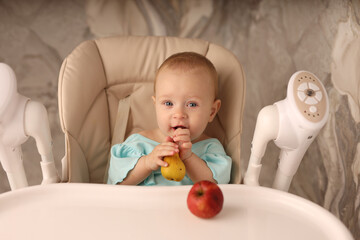 a baby in a feeding chair in a turquoise bodysuit eats a pear on her own. the concept of baby food. high-quality photography