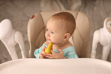 a baby in a feeding chair in a turquoise bodysuit eats a pear on her own. the concept of baby food. high-quality photography