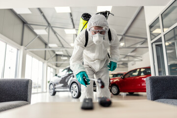 Close-up of an professional male person in protective white cloth and sprayer for cleaning and disinfecting the coronavirus high-risk area such as remotes. COVID19 prevention, pandemic situation