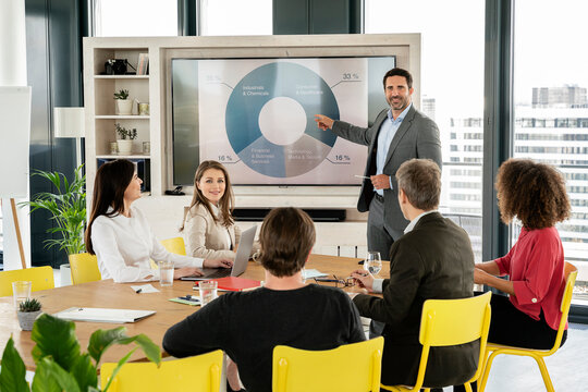 Male professional giving presentation on projection screen to colleagues at office - Powered by Adobe