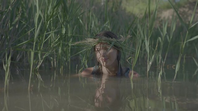 Beautiful water maiden with a wreath on her head, smiling comes out of the water