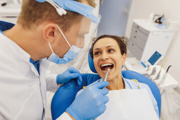 Dentist in protective mask examining client teeth
