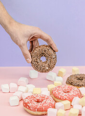 Hand taking colored donuts on pink and blue background with donuts and candy.