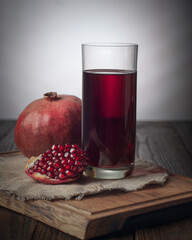 Pomegranate juice, with a slice of pomegranate, and a pomegranate in the background. All this stands on a wooden plank.