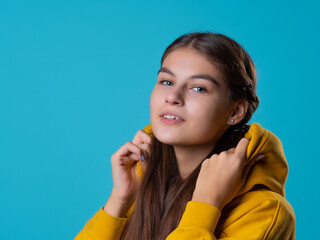 A beautiful young brunette in a yellow oversize hoodie, a positive student in a bright outfit, portrait on a blue background