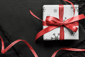 Christmas gift box with red ribbon on dark background. Flat lay, top view