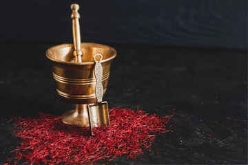 Raw organic red dried saffron spice on wooden background in vintage metal brass mortar with pestle, glass jar and tube - Powered by Adobe