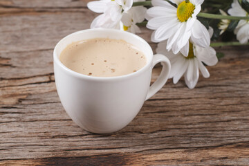 White coffee cup with hot cappuccino with latte on wooden background with white daisies