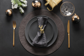 New Year and Christmas table setting with black plates, gold deer ring, gift and gold cutlery. Golden gilded decorations on black background. View from above. Flat lay. - obrazy, fototapety, plakaty
