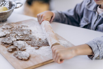 Little girl's hand making traditional Christmas cookies. Raw dough and cutters for the holiday cookies on a dark table.