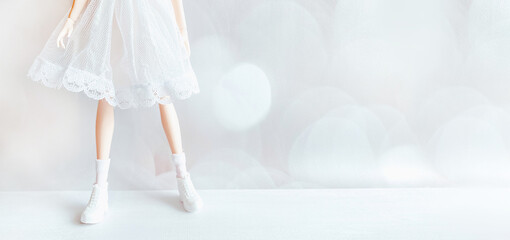 Legs of a doll in a white dress and shoes on a white background in the format of a banner
