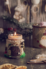 A burning handmade candle on the background of Christmas decor .