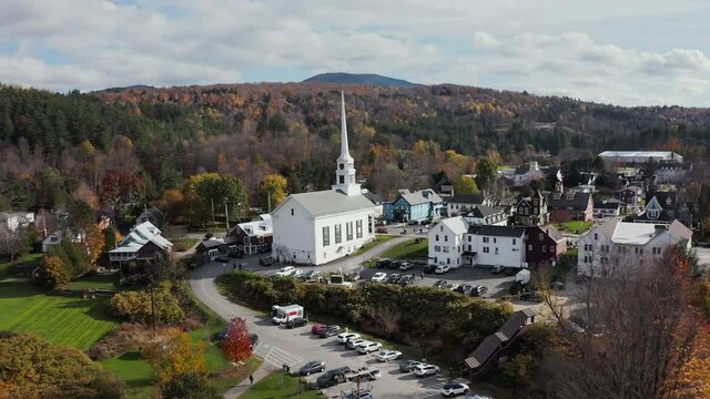 Flying towards white church in charming small town Stove in Vermont, New England.  Sunny day with clouds in autumn season.