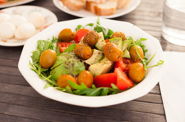 dish of fresh vegetables arugula, avocado, cherry tomatoes with olives on dining table