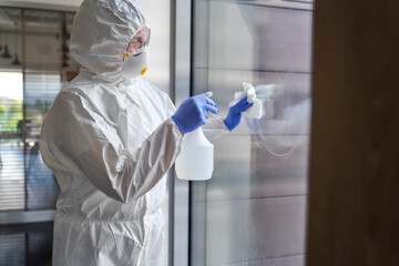 Female sanitation worker spraying chemical on glass while disinfecting office building