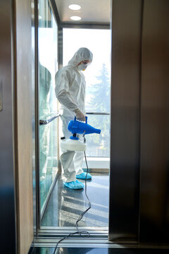 Female frontline worker using disinfection in office elevator