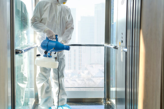 Female sanitation worker cleaning office elevator while spraying disinfection