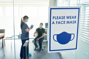 COVID-19 poster on door with patient and doctor in background at clinic