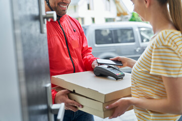 Woman paying through mobile phone while receiving pizza order from deliveryman at doorway