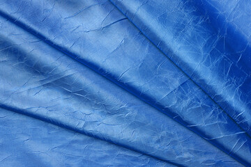 Draped crumpled silk of cobalt blue color background. Texture of folded coral blue shiny silk...
