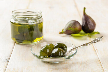 Delicious conserved unripe figs on a glass saucer, whole green figs in syrup jam jar and ripe...