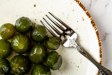 Top view of preserved whole green figs and dessert fork on a white porcelain plate. Sweet jam of...
