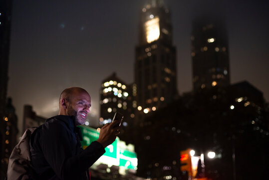 USA, New York, New York City, Smiling man using smart phone in city at night