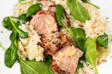 Pork tenderloin medallions on risotto with parmesan and spinach leaf,closeup.