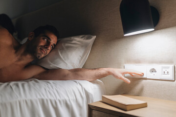 Mid adult man turning off light while lying on bed