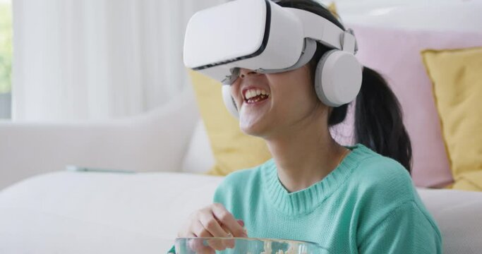Asia people teen girl enjoy play AR media online sitting laugh humor joy at cozy sofa relax eat food wear eye glasses tv display fun video game in cyber app. Overjoy smile in VR augmented film.