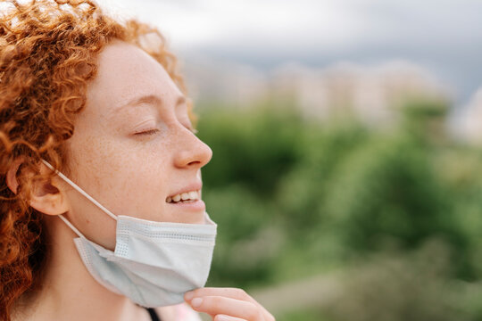 Young Woman With Eyes Closed Removing Protective Face Mask During Pandemic